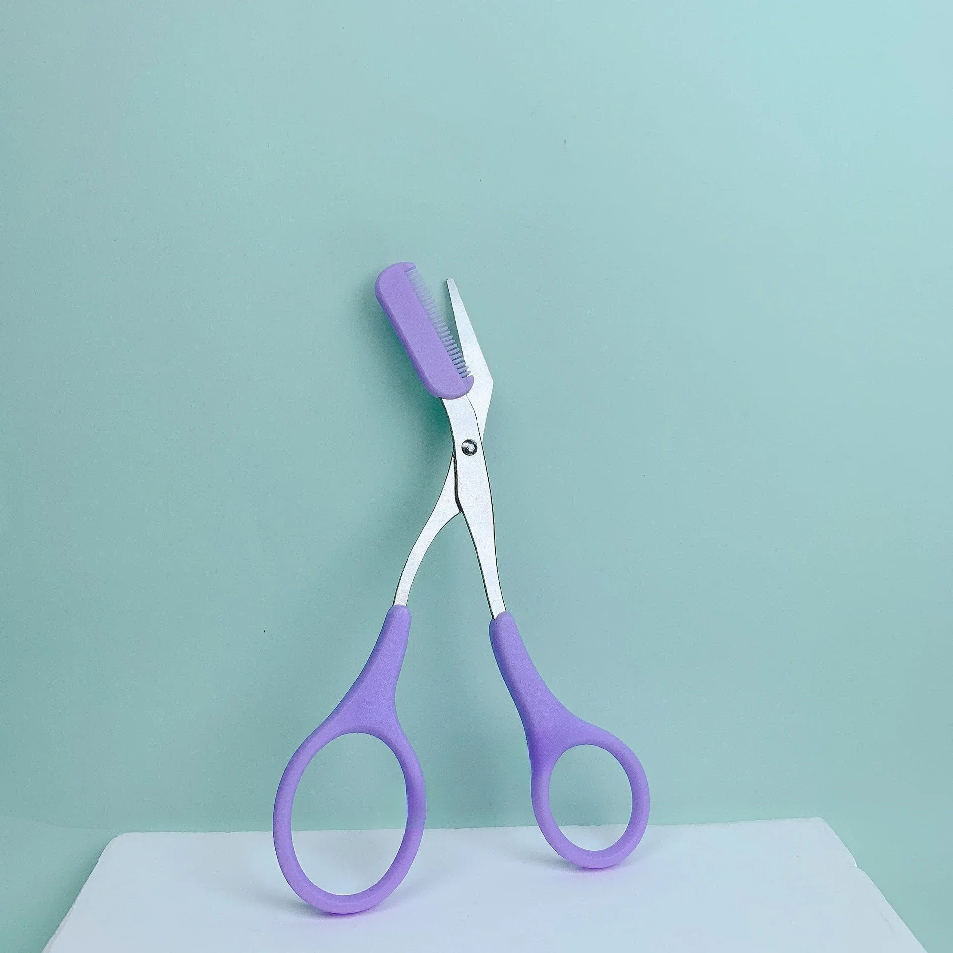 Eyebrow Trimming Scissors with Built-in Comb displayed on a light background, featuring purple handles and precision blades.
